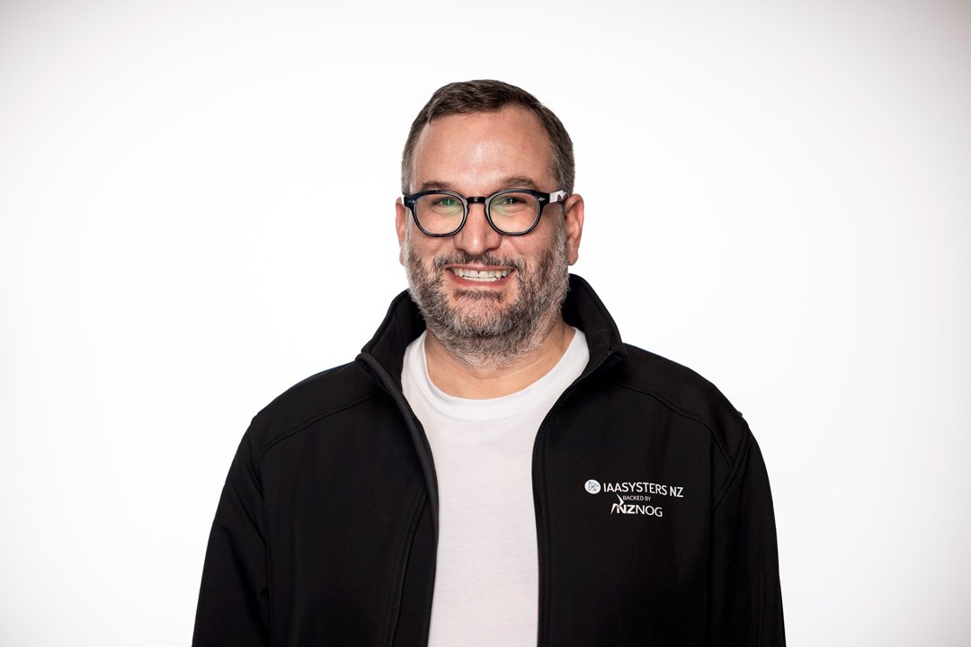 Nathan - founder and principal consultant at Searchlight, a smiling man with glasses, a beard, wearing a black jacket and a white shirt, standing against a white background.