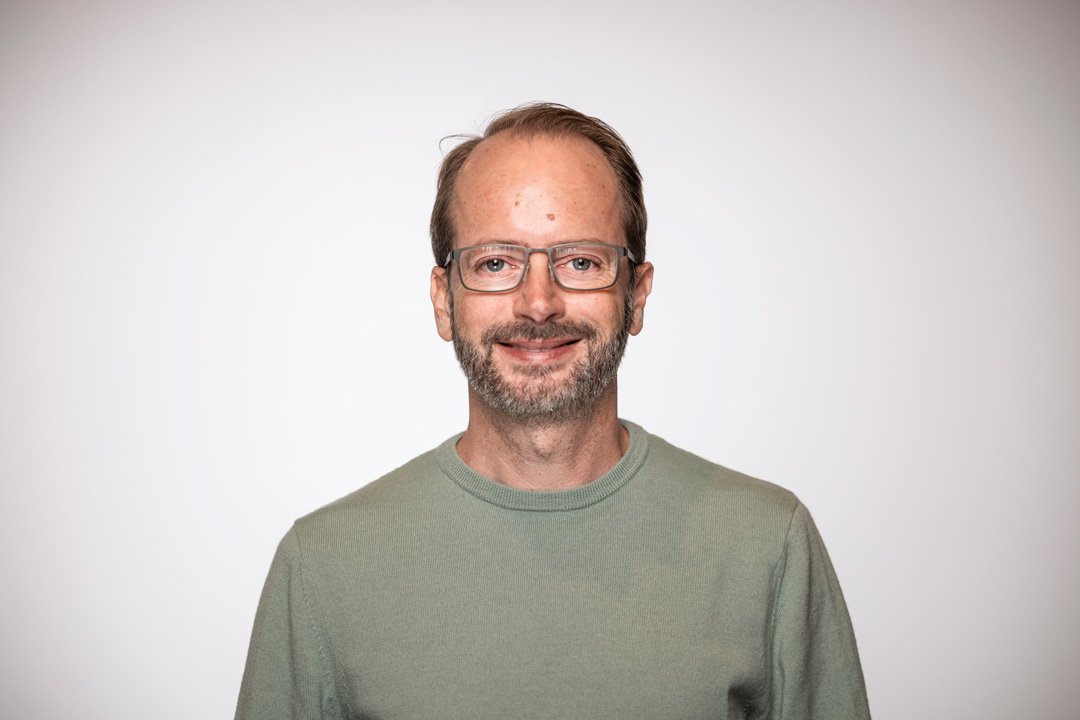 Dave, senior consultant at Searchlight, digital infrastructure specialists in Auckland, a man with glasses, short brown hair, and a beard, wearing a green shirt, smiling against a plain white background.