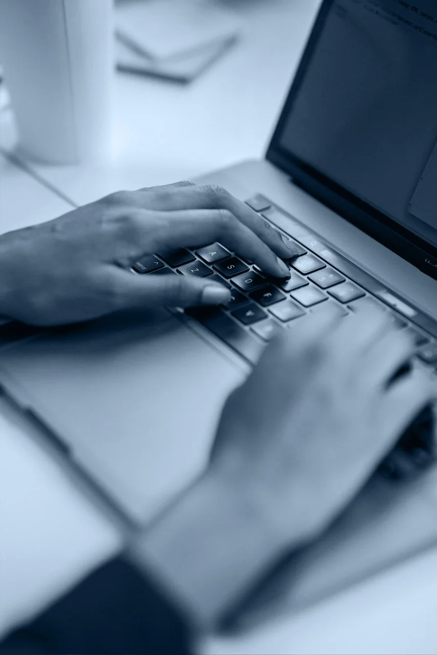 Close-up of a person's hands typing on a laptop keyboard in a modern office setting, working with Imera, hosted email NZ