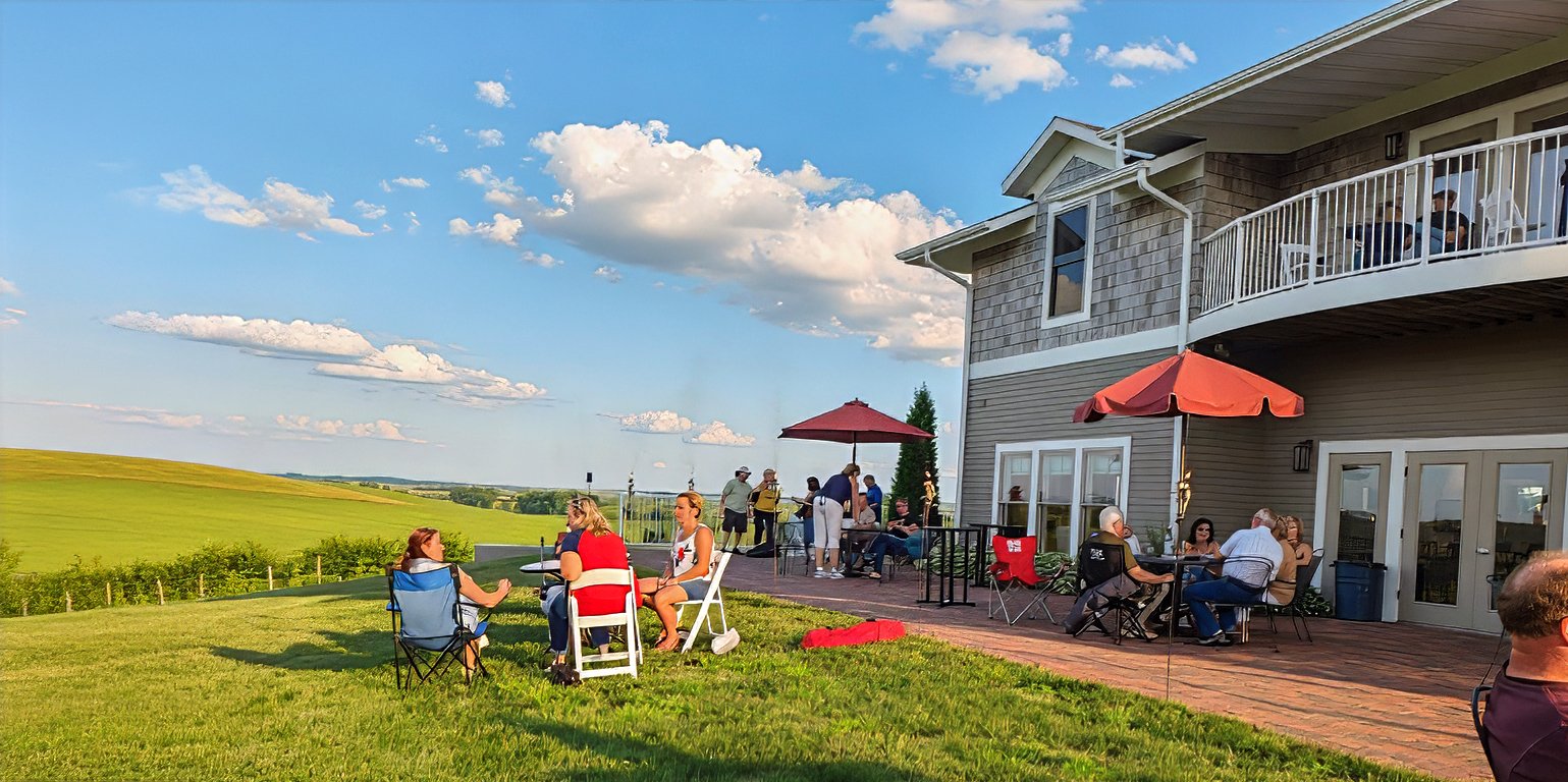 People Gathering on a patio and lawn outside a house, enjoying a sunny day with clouds in the sky.