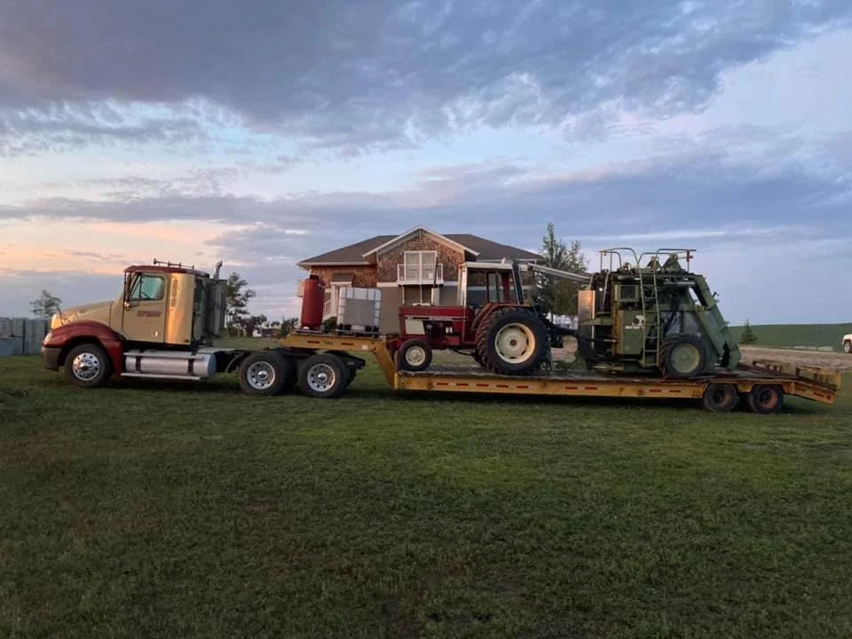 Flatbed truck transporting a house, with a tractor and a lawnmower loaded on the house.