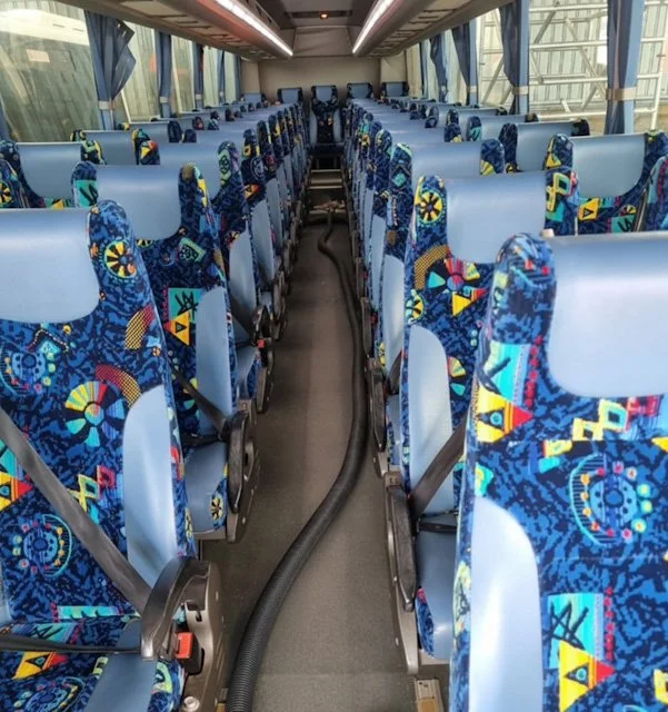 Interior of a bus with rows of blue patterned seats and a central aisle.