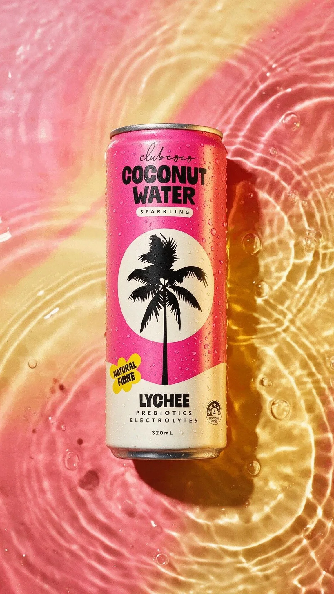 Pink can of Club Coco Coconut Water with a black palm tree illustration, placed on a pink and yellow surface with water ripples and bubbles.