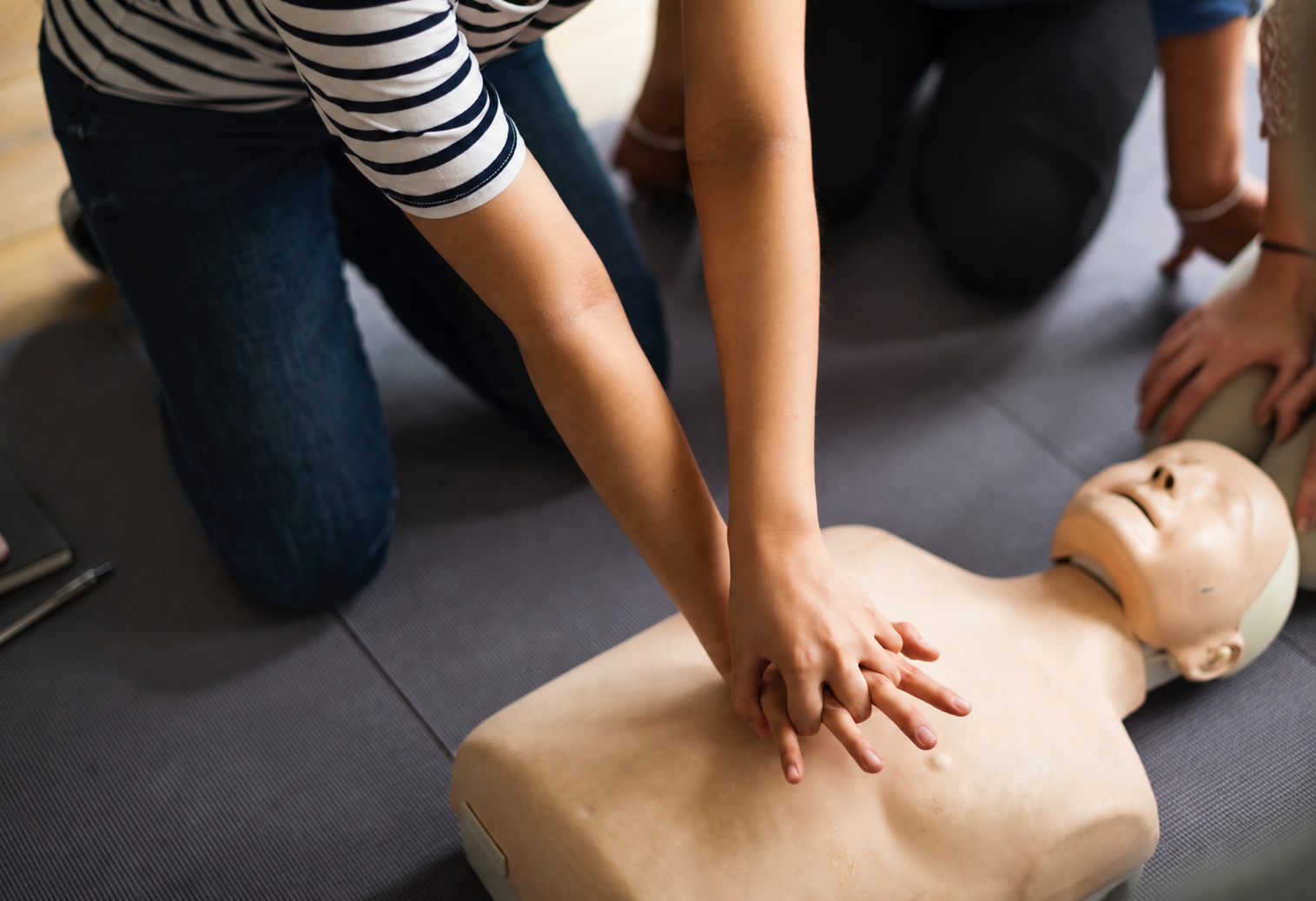 People practicing CPR on a training dummy on a gray mat.