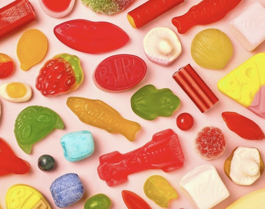 Assorted colorful candies and gummies on a pink background.