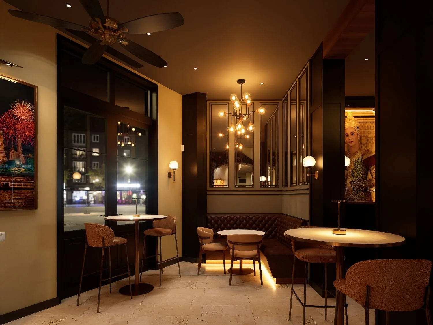 Interior of a cozy, dimly lit cafe with round tables, upholstered chairs, wall sconces, a chandelier, and artwork on the walls.