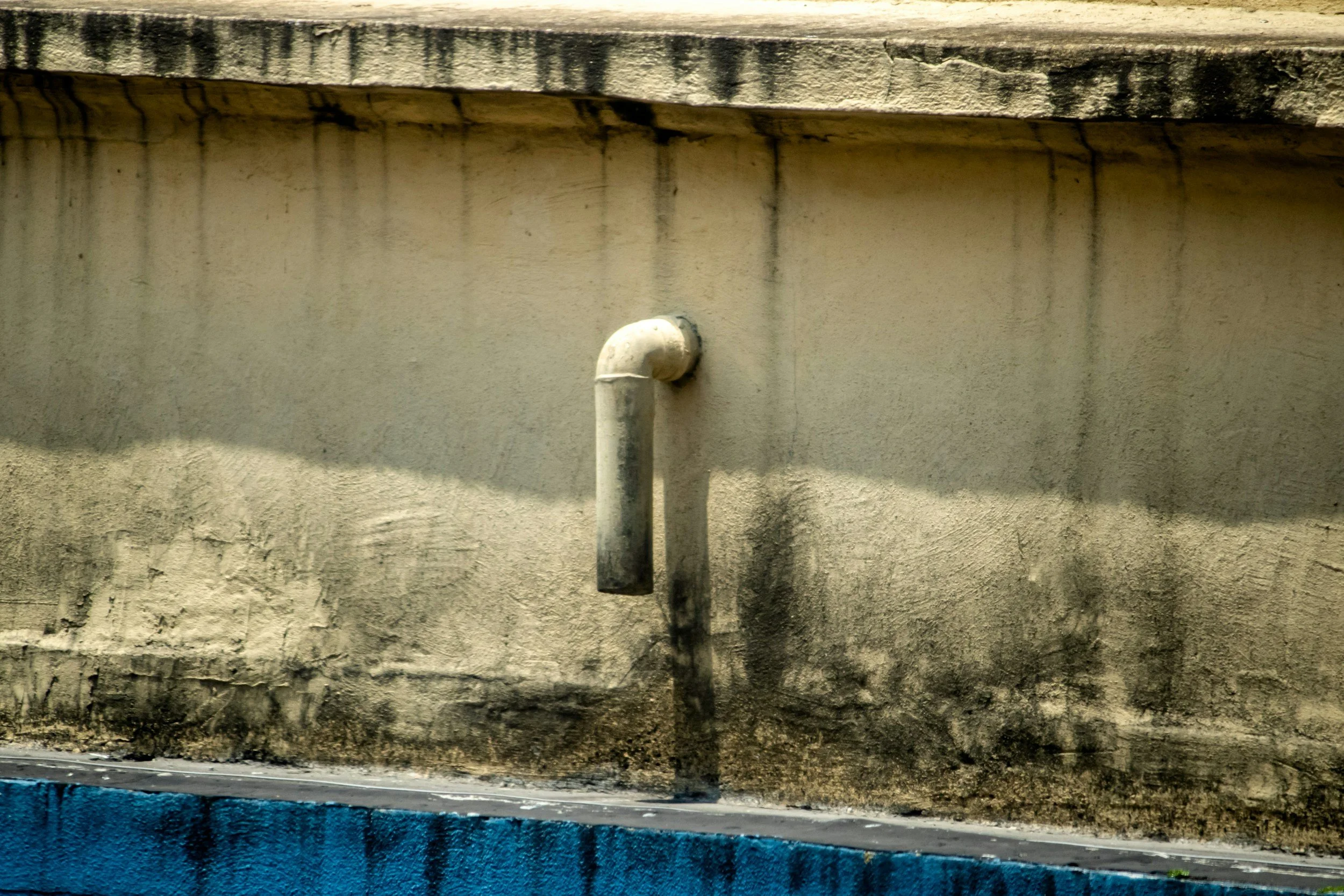 Close-up of a plumbing pipe protruding from a textured wall with peeling paint and black stains. Water Damage Restoration Australia