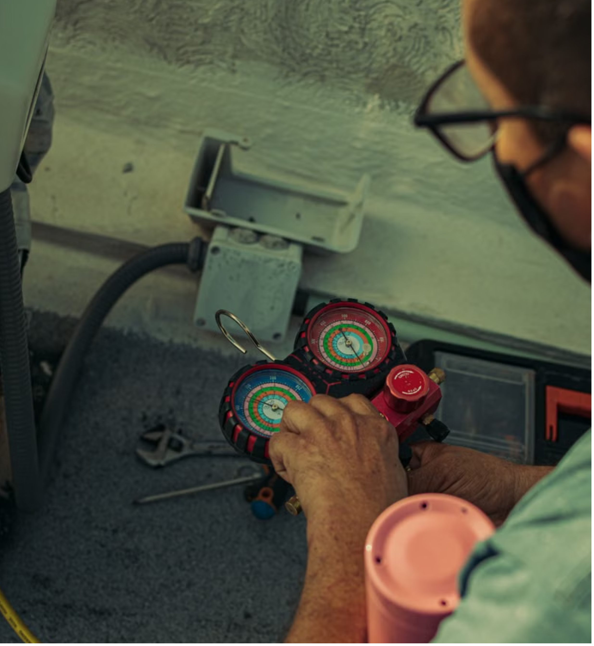 A worker using refrigeration gauges connected to a pink expansion tank in an HVAC system.