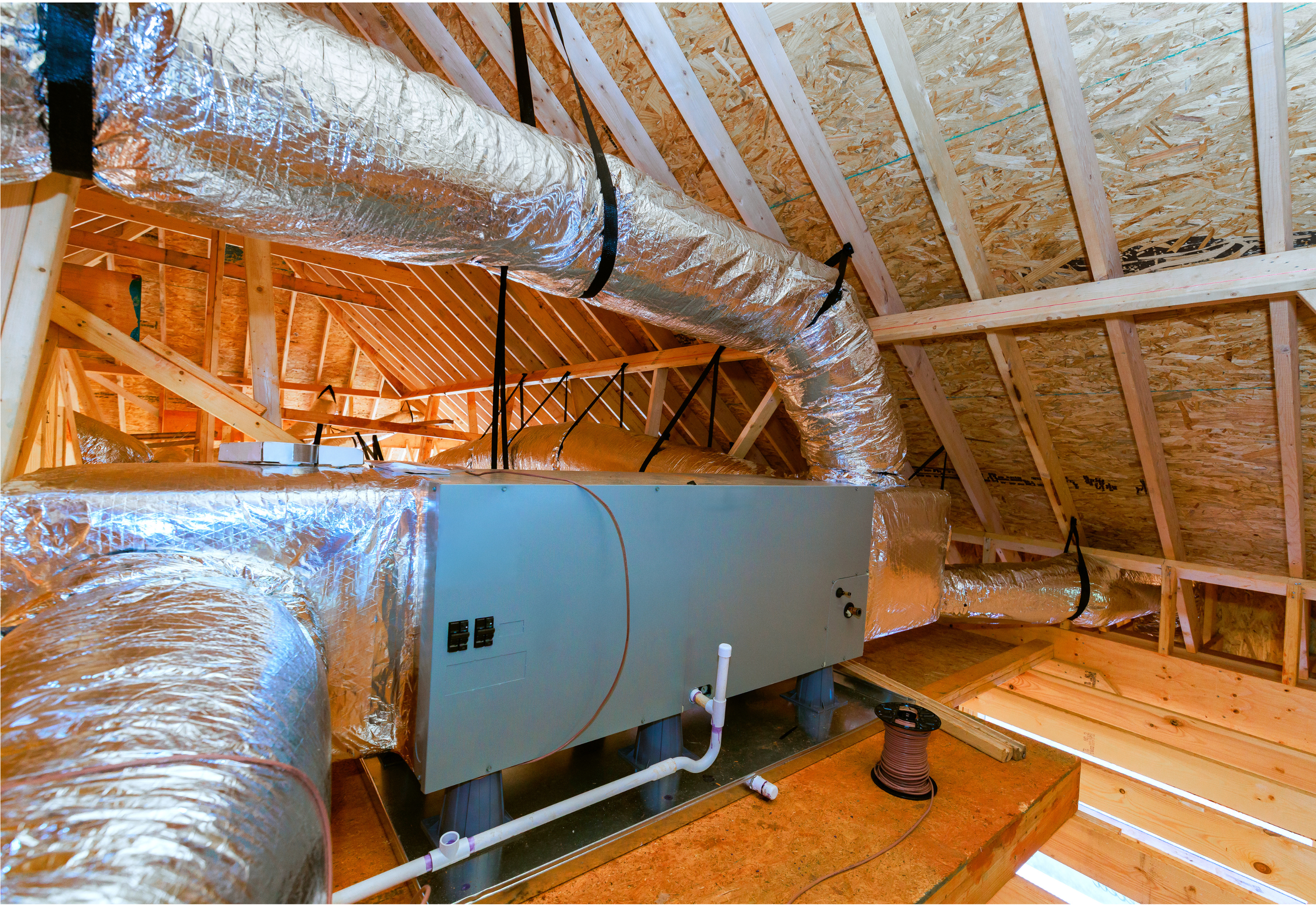Attic with ventilation ductwork and a furnace or HVAC system installed on a wooden floor, with unfinished wooden ceiling framing and insulation visible.