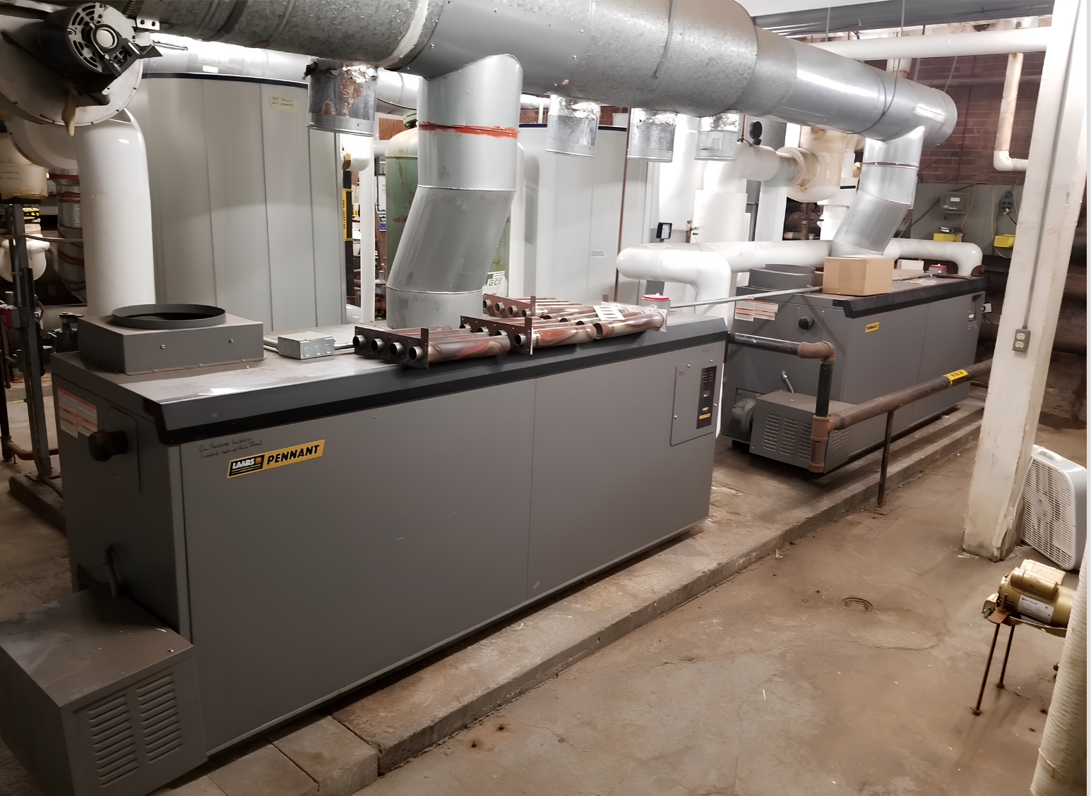 Industrial machinery in a factory setting, with multiple pipes, some labeled 'Pennant,' and various metal components on a concrete floor.