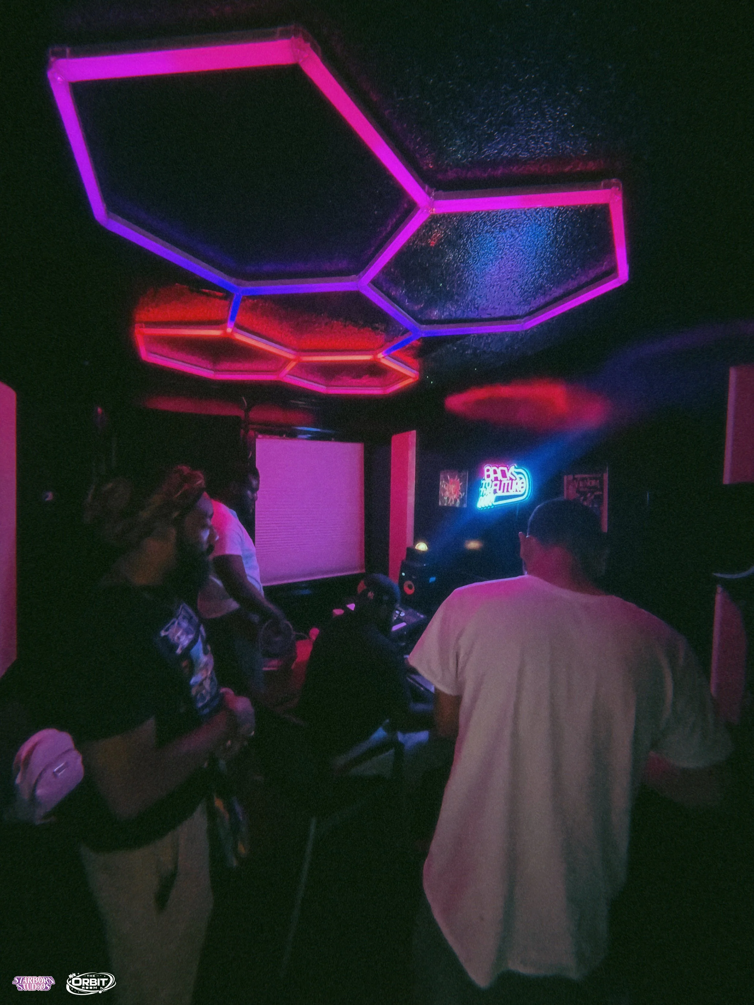 Dimly lit nightclub with neon pink, purple, and red hexagon-shaped ceiling lights, people gathered around DJ equipment, and a neon sign that says 'Back to the 80s'.