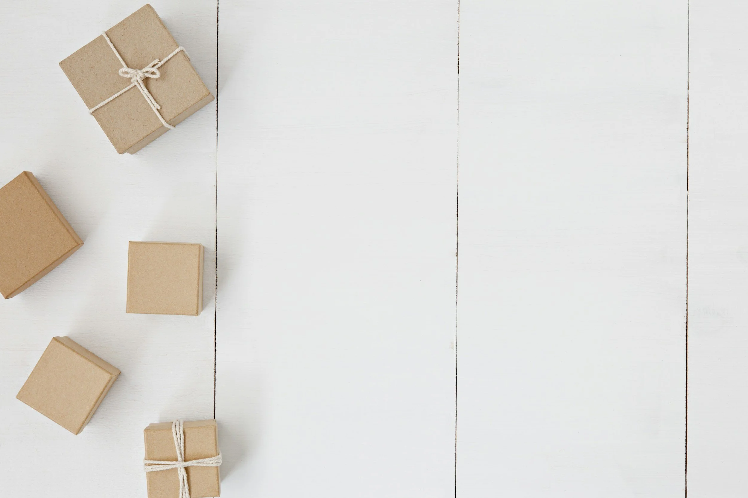 Multiple small gifts wrapped in brown paper with white string, placed on a white wooden surface.