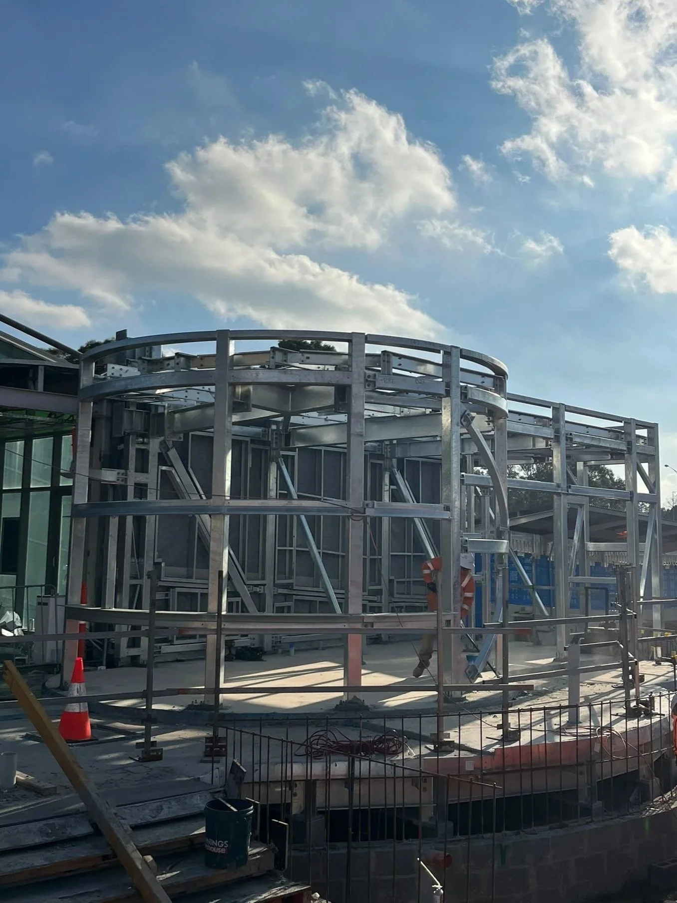 Construction site with a partially built metal framework structure under a blue sky with scattered clouds.