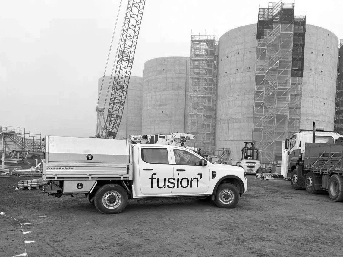 Construction site with large concrete silos, construction vehicles, and scaffolding.
