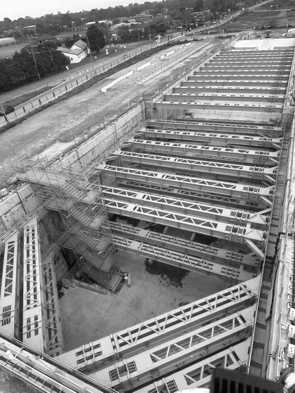 View of a construction site with large metal frameworks, scaffolding, and stairs, viewed from above.