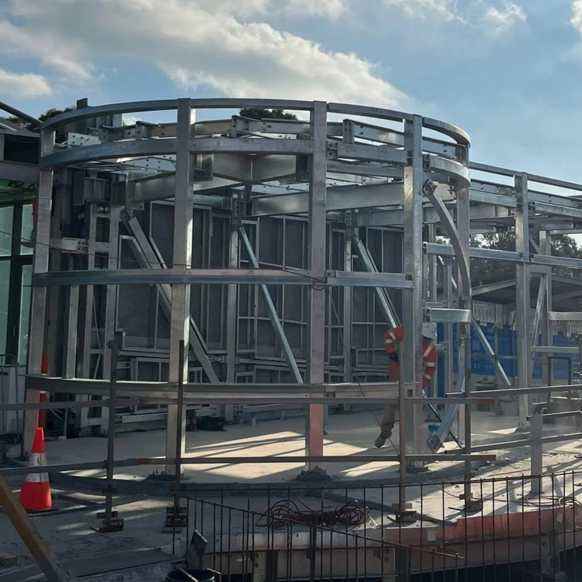 Construction workers assembling a metal framework for a building or structure outdoors on a sunny day.