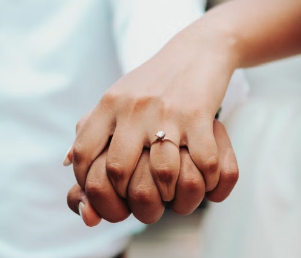 Close-up of two hands holding each other, with one hand wearing an engagement ring.