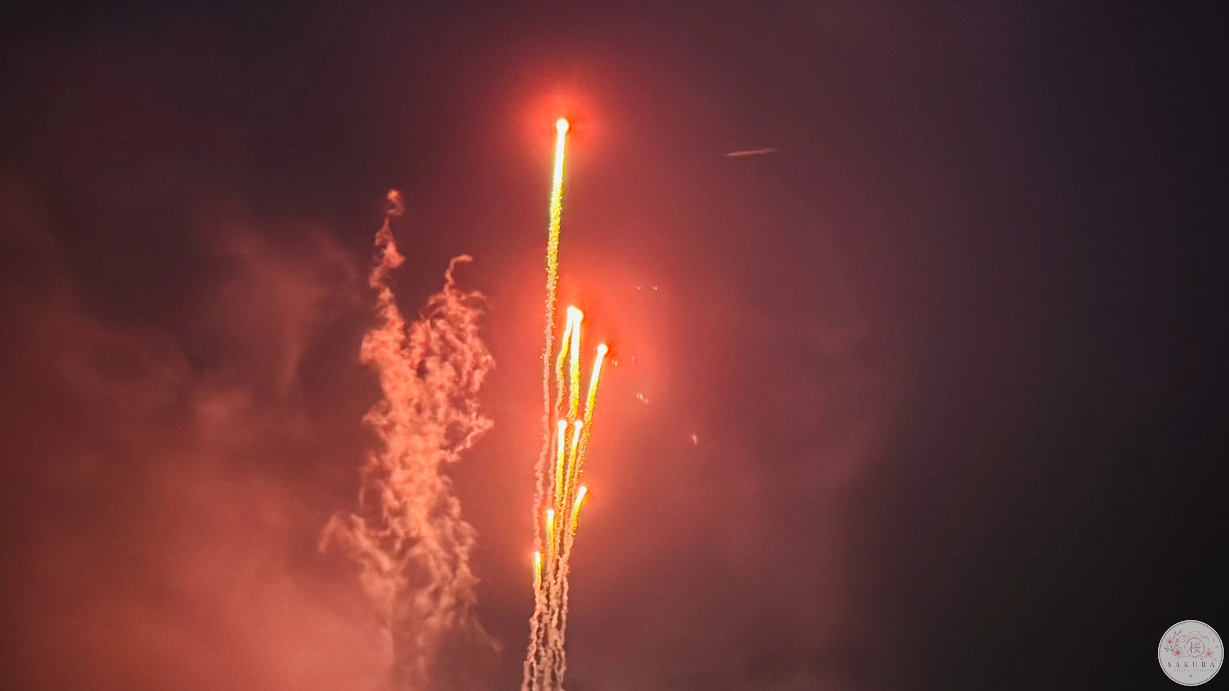 Fireworks streaking across the night sky with bright red-orange glow and smoke.