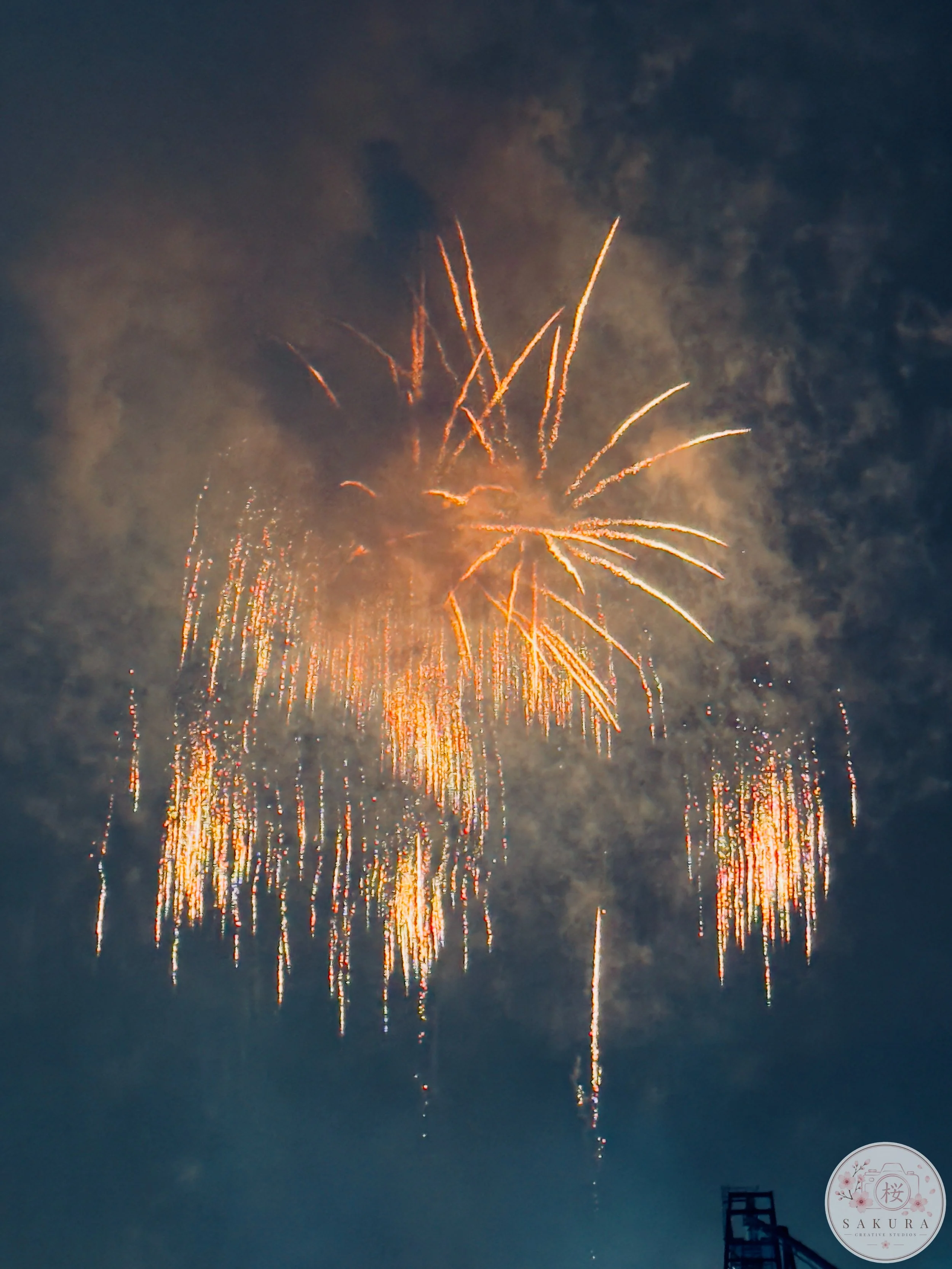 Fireworks lighting up the night sky with orange and yellow streaks against dark clouds.