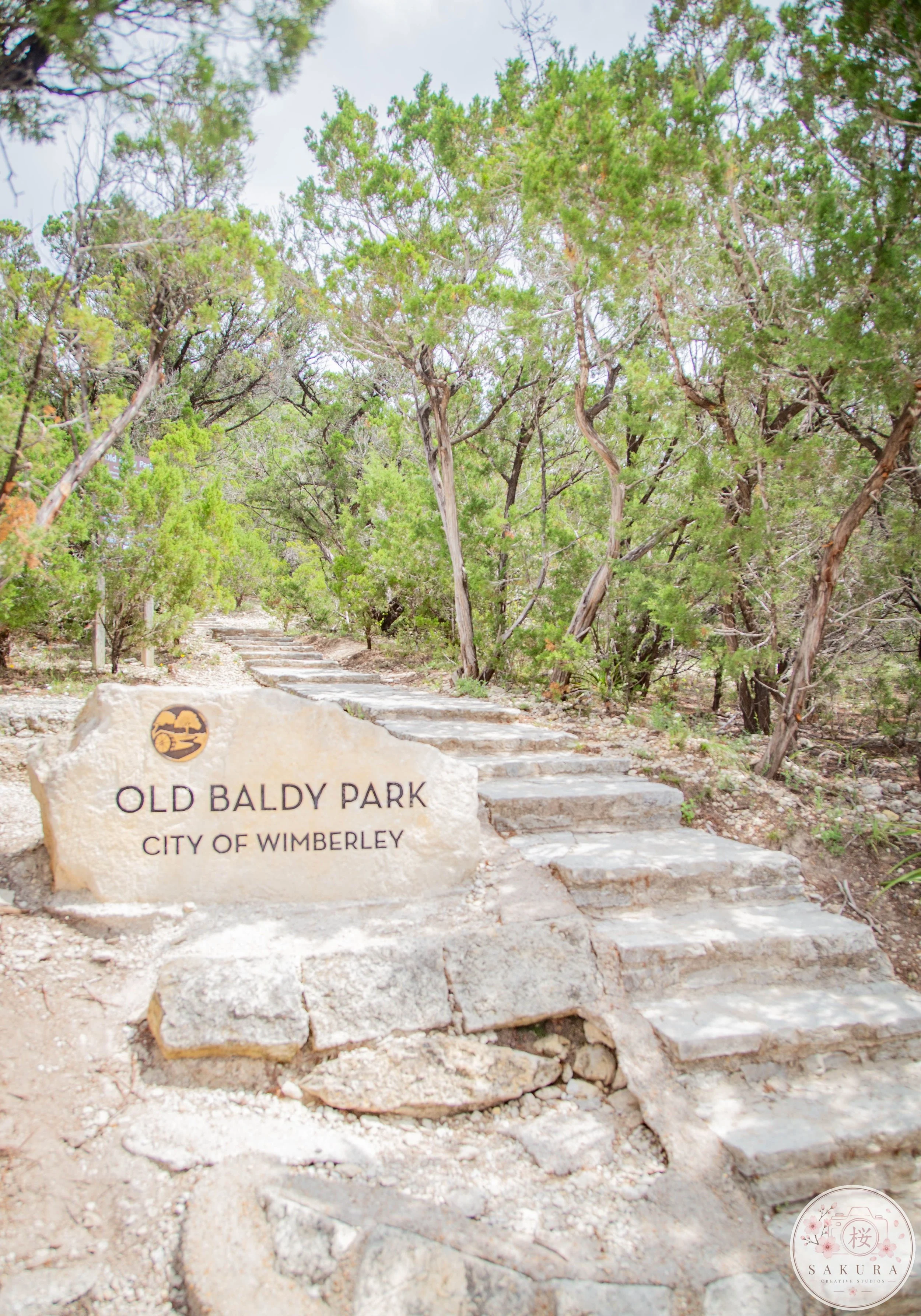 Stone sign at Old Baldy Park in the City of Wimberley, with stone steps and trees in the background.