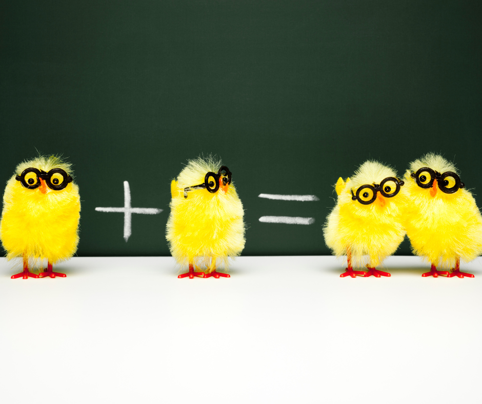 Three small yellow plush chicks with glasses, standing on a white surface in front of a chalkboard with a math addition equation written in chalk, plus and equals signs, and two of the chicks are leaning on each other.