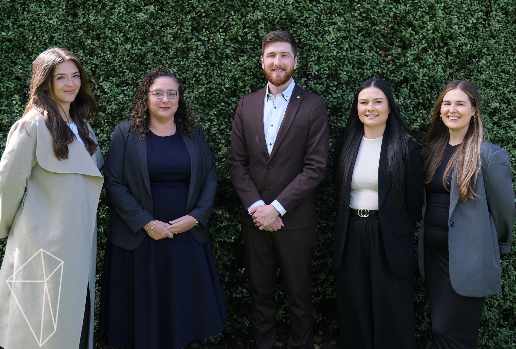Citrine Advisory staff professionally dressed people standing outdoors in front of a green hedge, smiling at the camera.