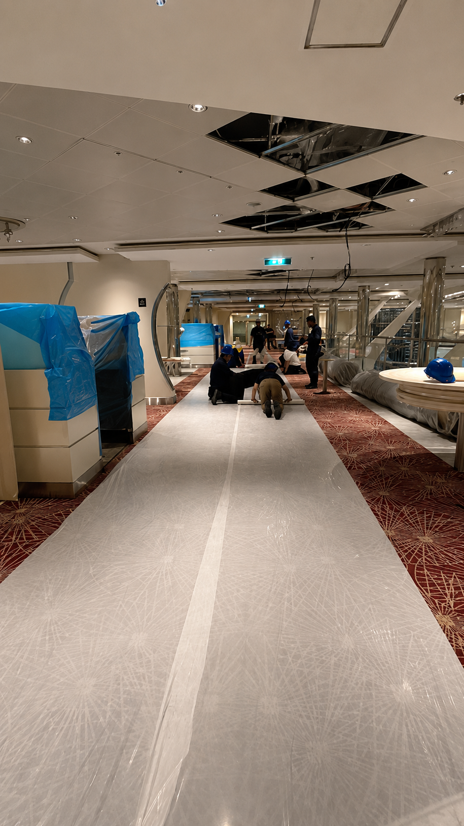 People working on installing a new carpet on a hotel or apartment building hallway, with tools and construction materials around.