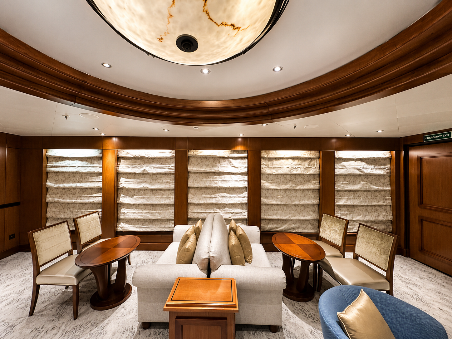 Elegant, wood-paneled lounge with cream and blue seating, multiple windows with textured beige curtains, and a large, oval ceiling light.