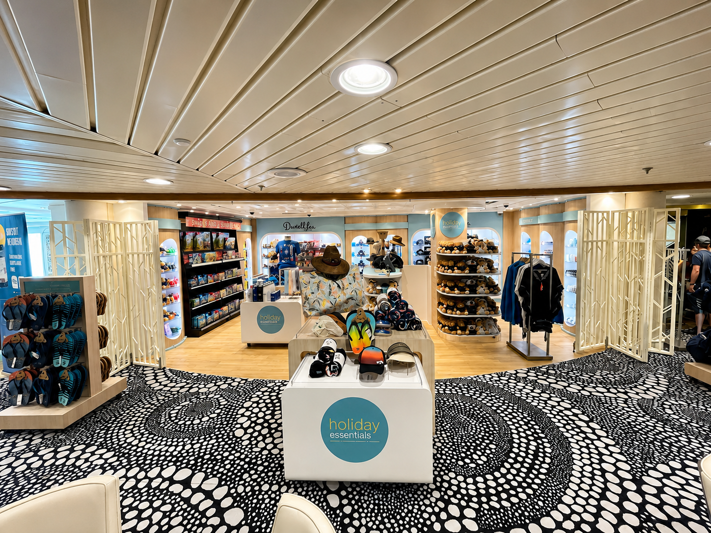 A retail store with a variety of summer accessories and souvenirs displayed on white shelves and tables, including hats, hats, sandals, and sunglasses, with a patterned black and white carpet in the foreground.
