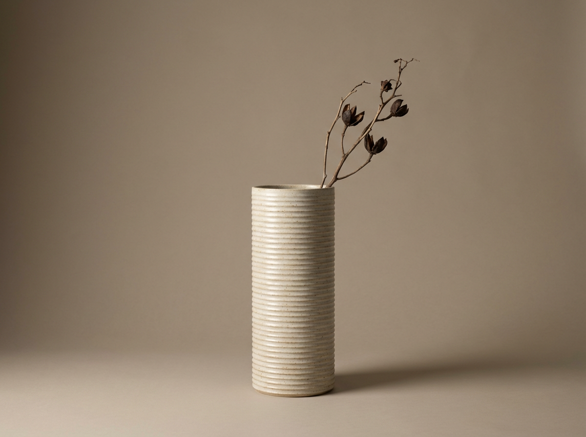 A tall, cylindrical, ribbed ceramic vase with dried branches and leaves against a neutral background.