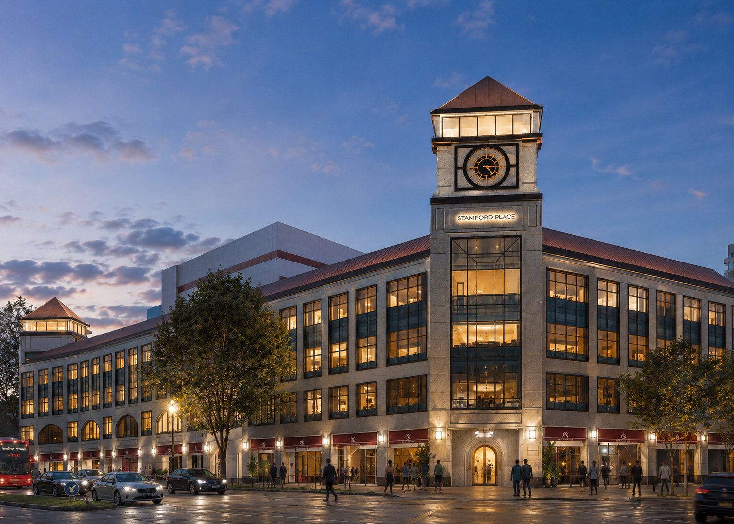Exterior view of a multi-story building called Stamford Place with a prominent clock tower, lit windows, trees, pedestrians on the sidewalk, and cars on the street during evening twilight.