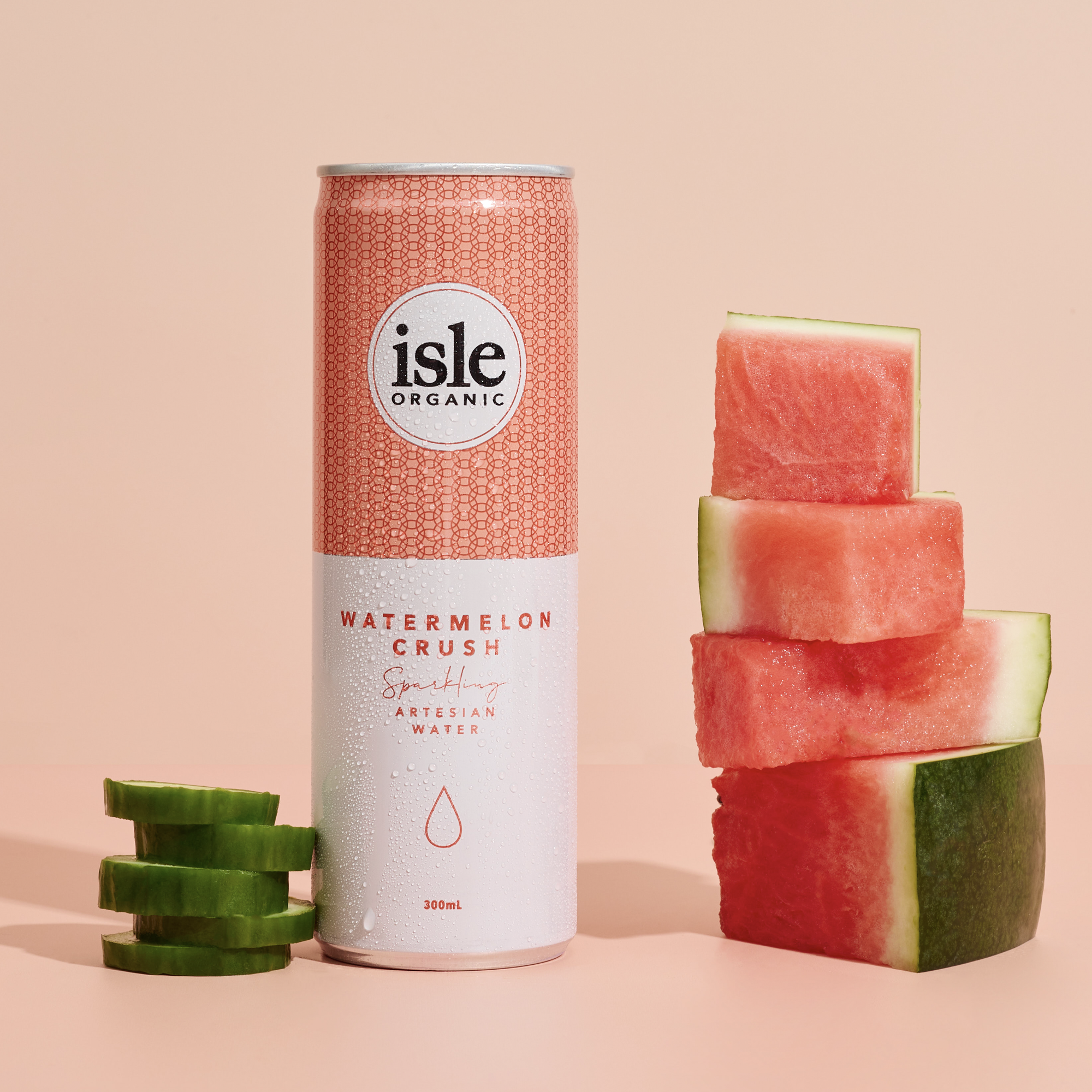 A can of Isle Organic Watermelon Crush sparkling water positioned between slices of cucumber and watermelon against a pale pink background.