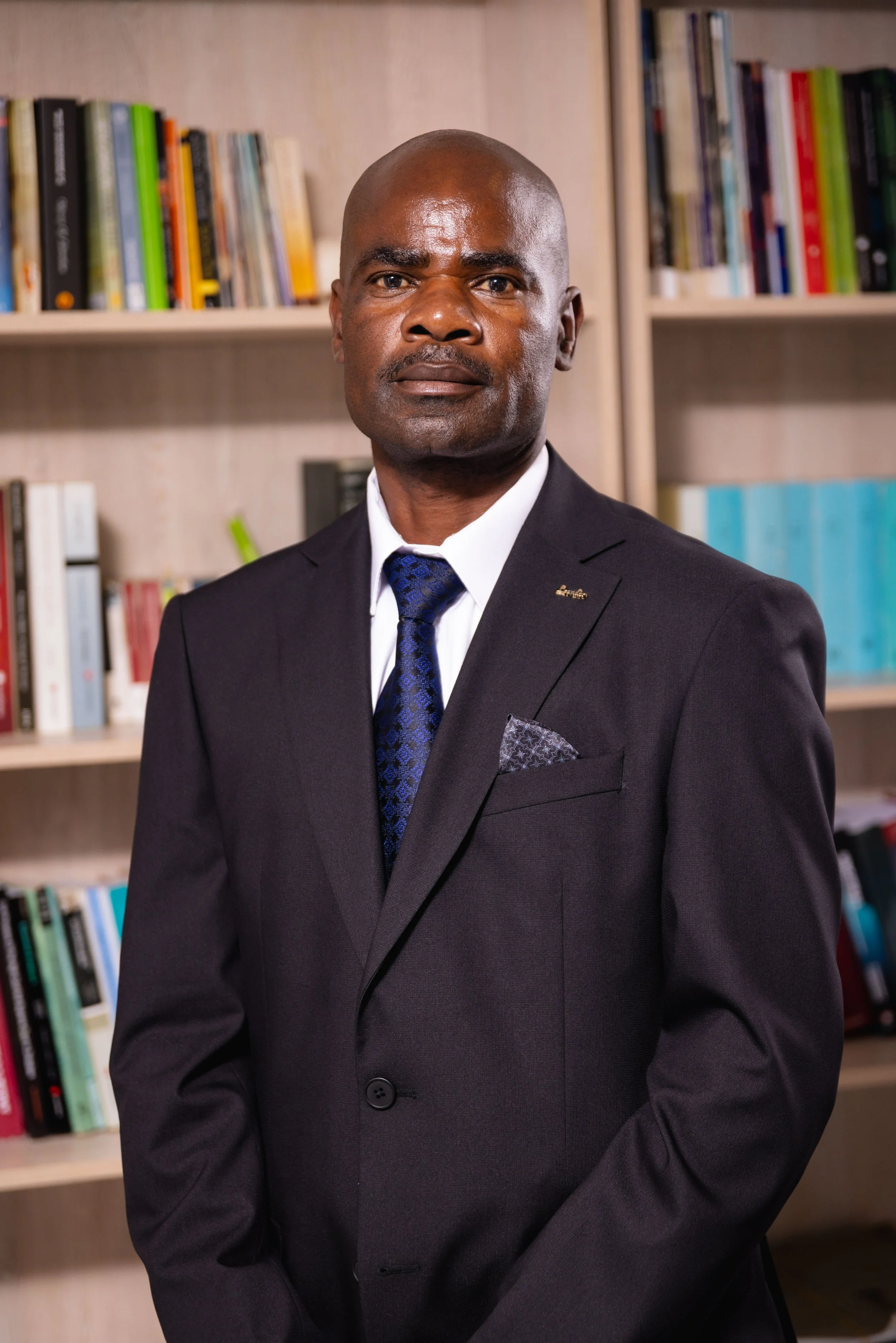 A man in a suit standing in front of bookshelves filled with books.
