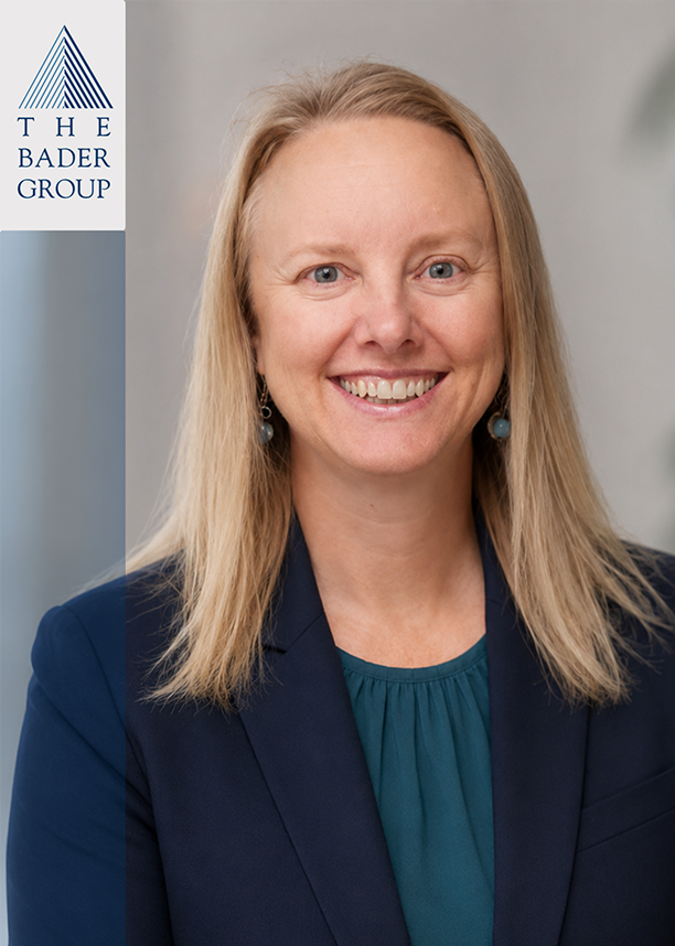 A professional woman with long blonde hair, blue eyes, wearing a navy blazer and teal blouse, smiling in front of a neutral background with a logo for The Bader Group on the left.