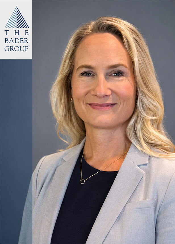 Professional woman with blonde hair, wearing a light gray blazer and black top, standing against a gray background with logo of The Bader Group in the top left corner.