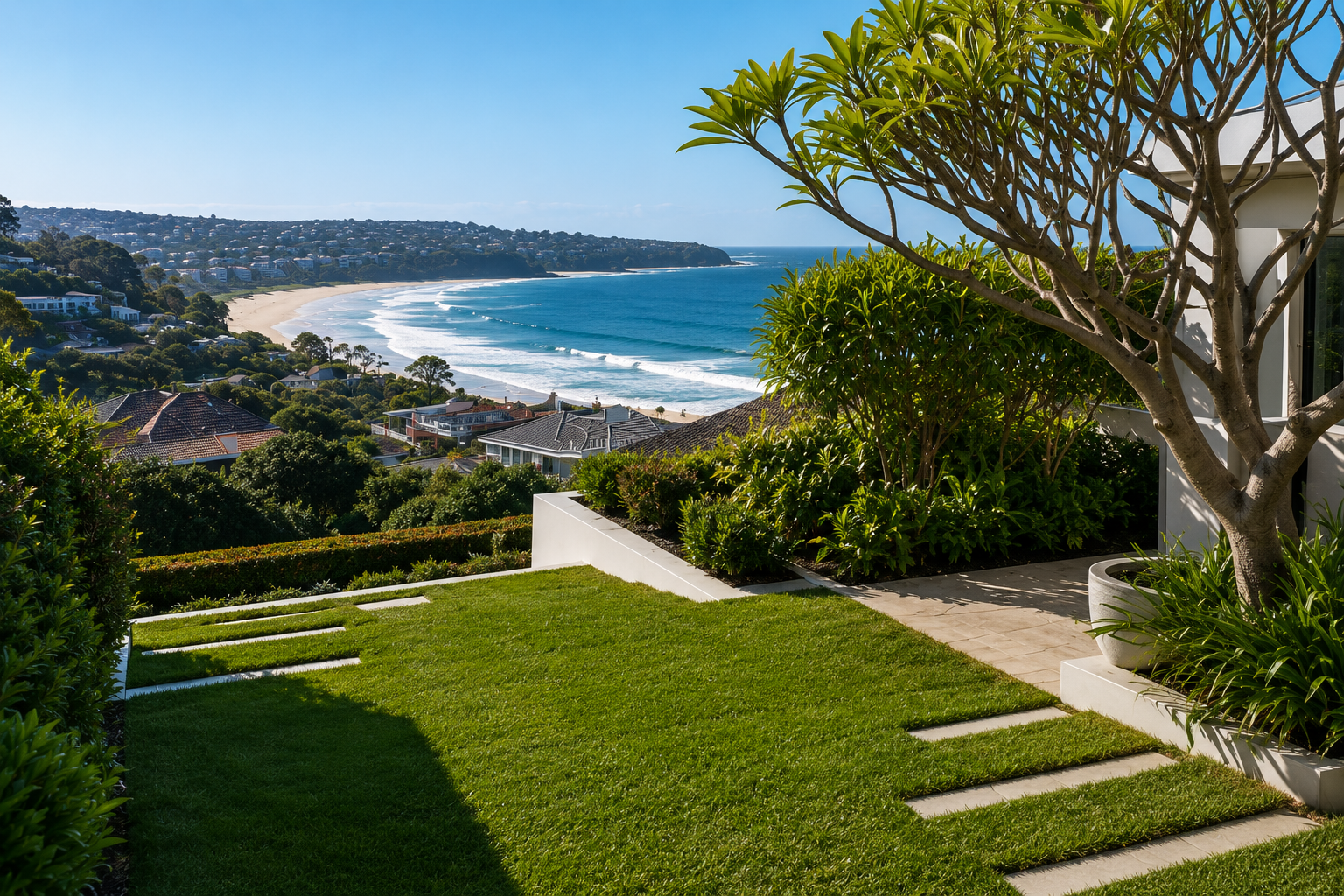 A landscaped backyard with green grass, stepping stones, and bushes overlooks a coastal view of a beach, ocean, and hillside houses under a clear blue sky.