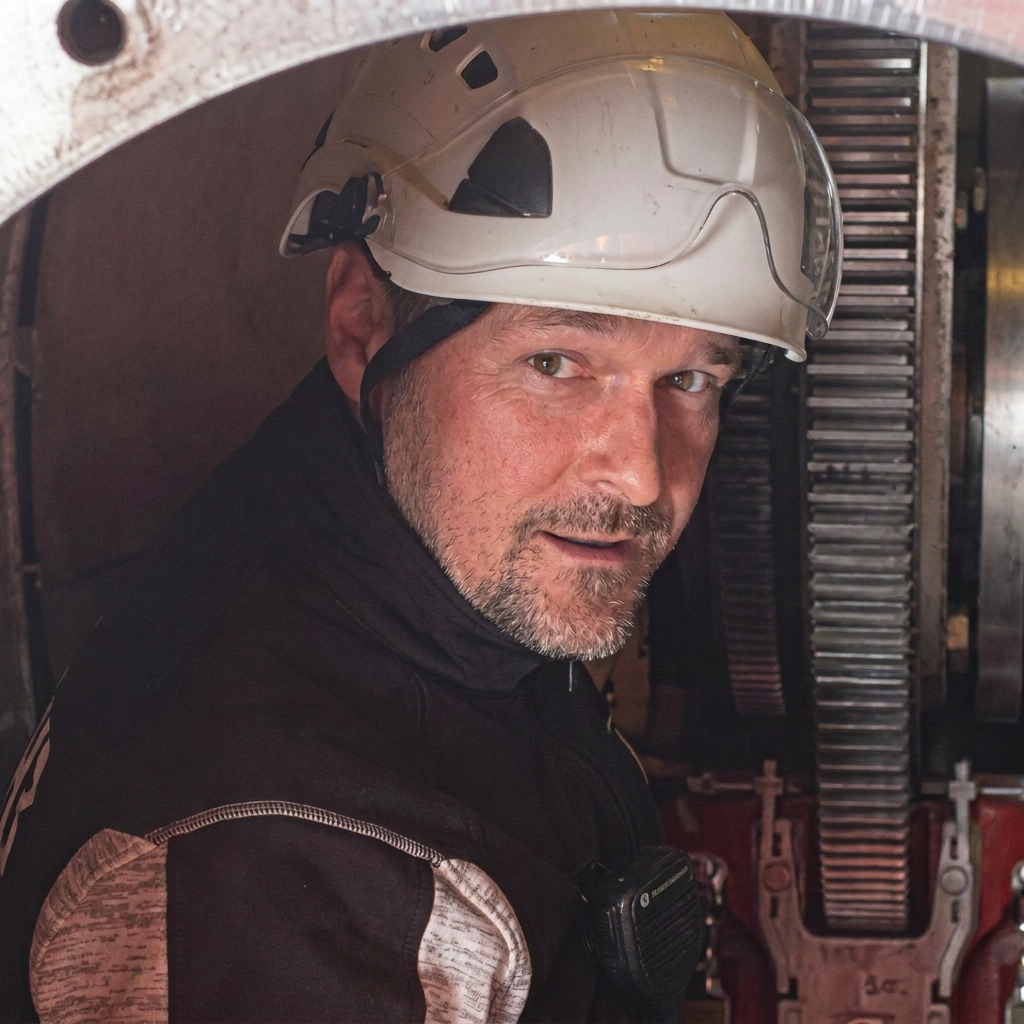 Firefighter wearing a white helmet with the brand PETZL, looking at the camera, inside a fire truck or emergency vehicle.