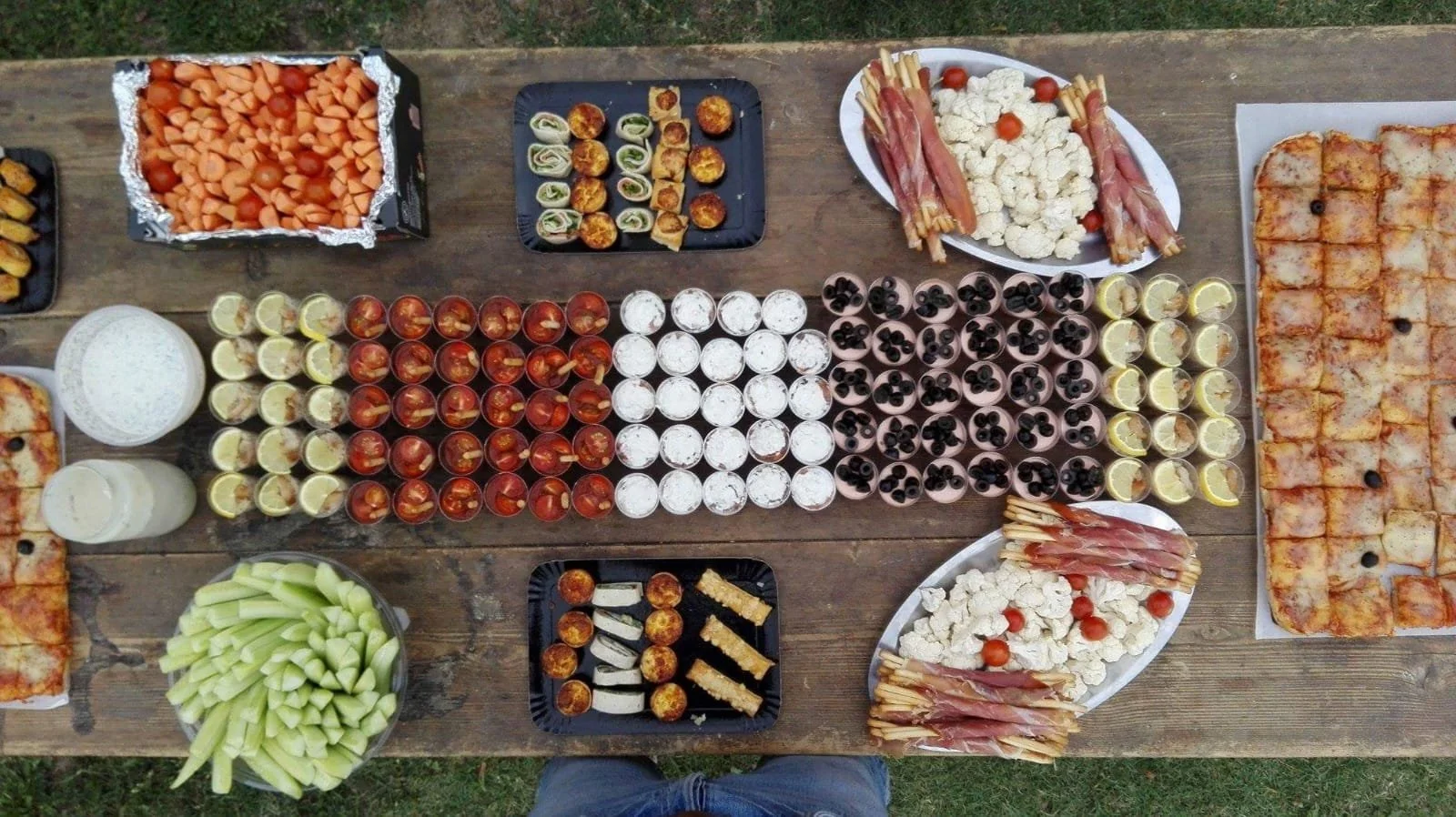 Repas avec divers amuse-bouches, fruits, boissons et pizza sur une table en bois.
