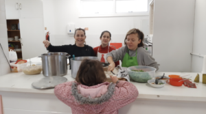 Four children in a kitchen, three standing behind a counter and one facing away, engaging in cooking or baking activities.