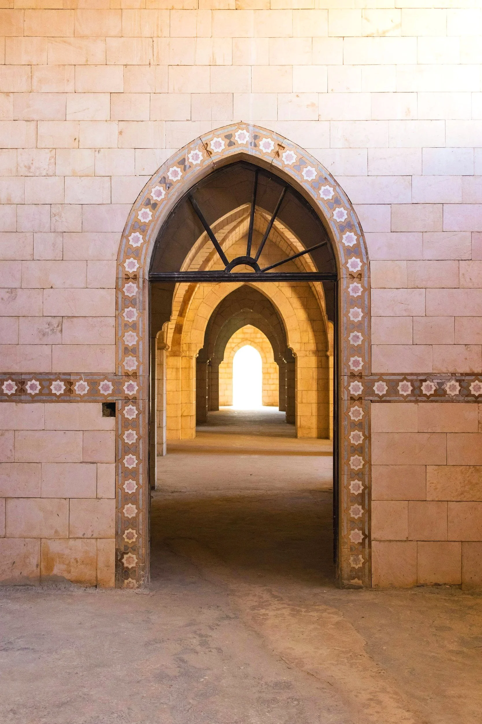 A series of arched doorways in a beige stone building, with decorative tilework framing each arch, leading to a bright outdoor area.