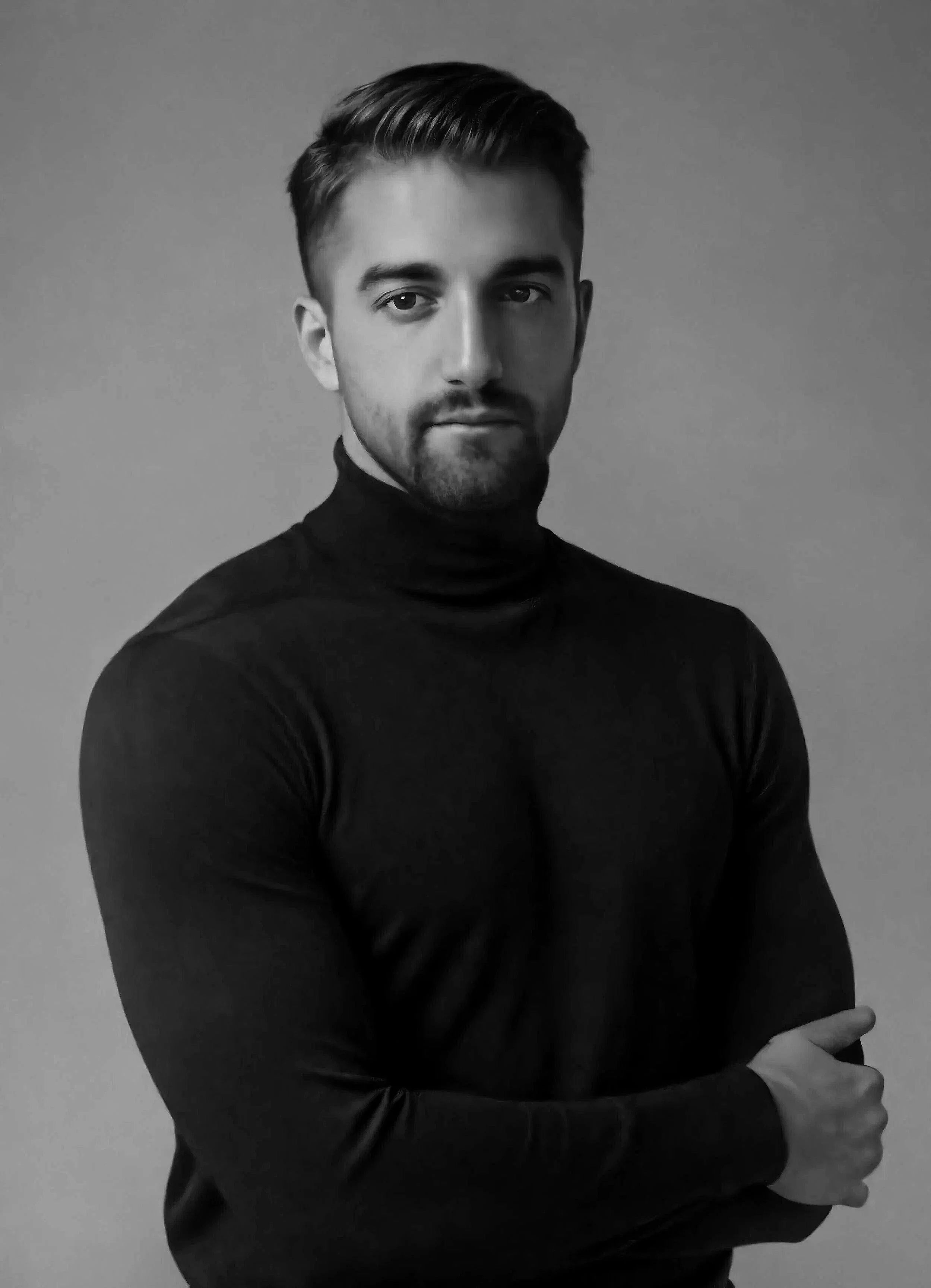 Ritratto di un uomo con capelli corti e barba, indossa una maglietta a collo alto, scatto in bianco e nero.