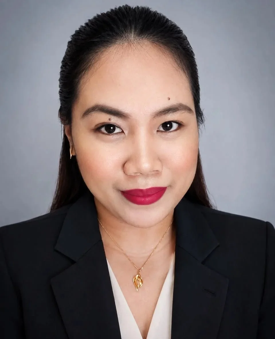 A professional woman with dark hair, red lipstick, and light makeup, wearing a black blazer and a gold necklace, against a gray background.
