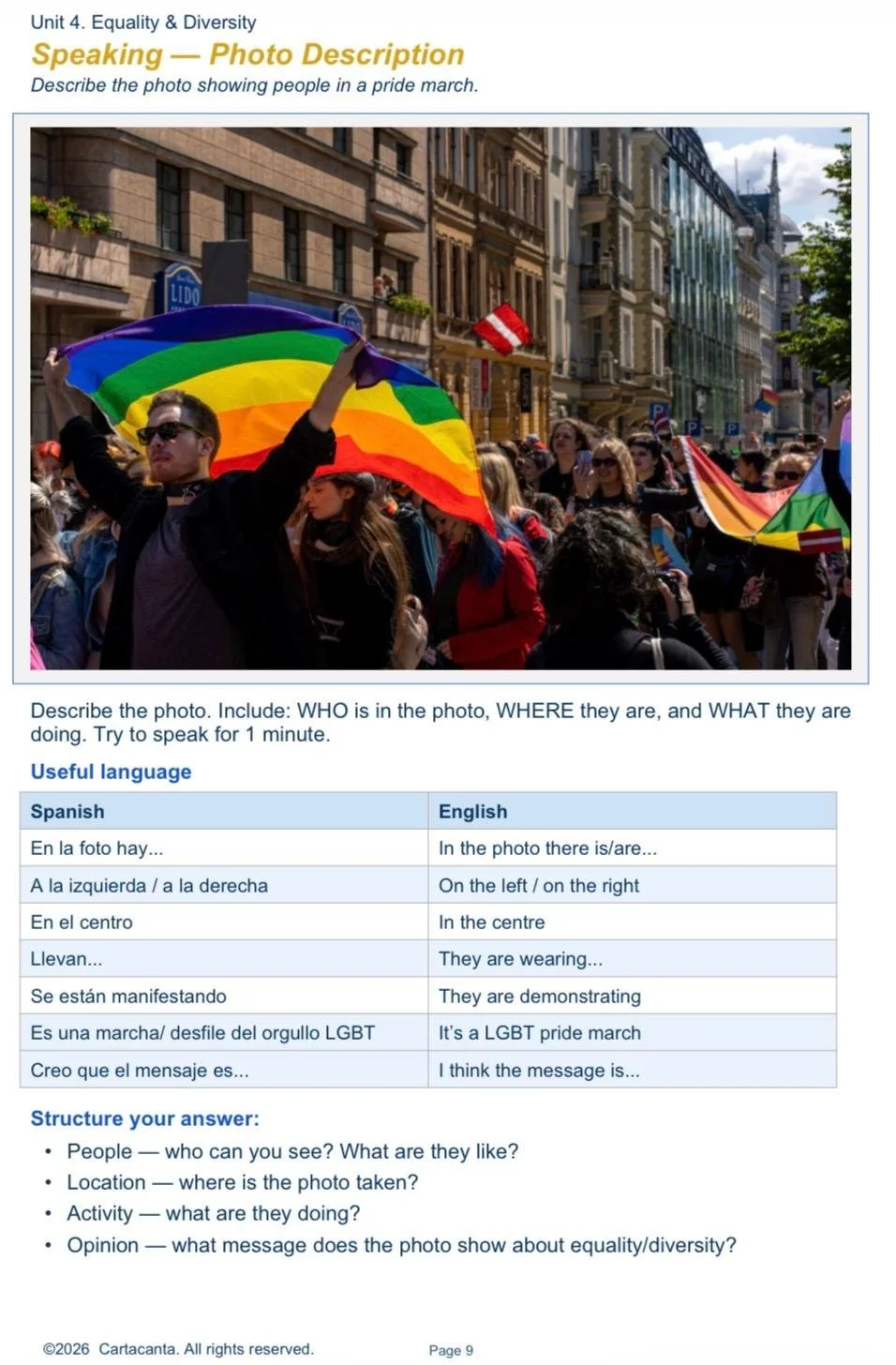 People participating in a pride march on a city street, holding rainbow flags and banners, with colorful buildings and a partly cloudy sky in the background.
