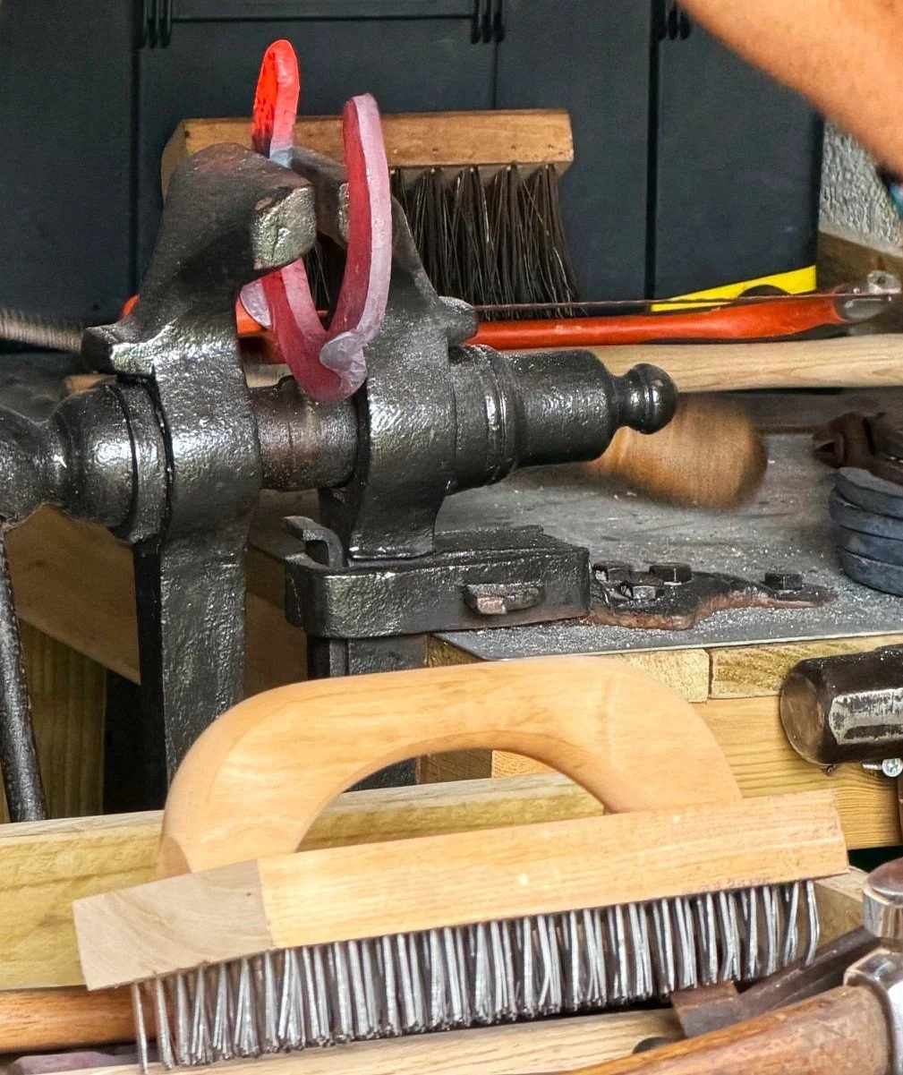 Close-up of a workbench with various tools, including a vise, a wire brush, a hammer, and a chisel.
