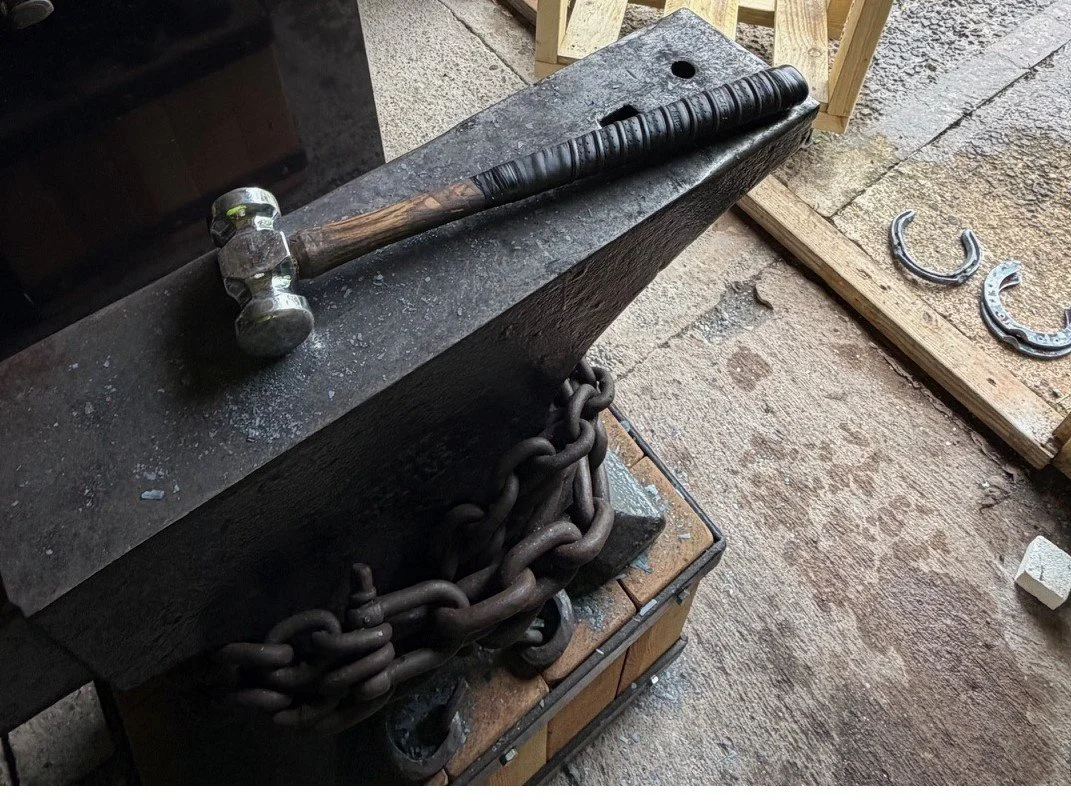 Blacksmith hammer resting on an anvil with chains hanging underneath, in a workshop setting.