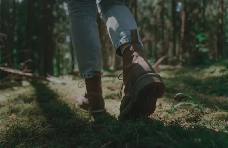 Close-up of a person walking in a forest, showing their boots and part of their jeans.
