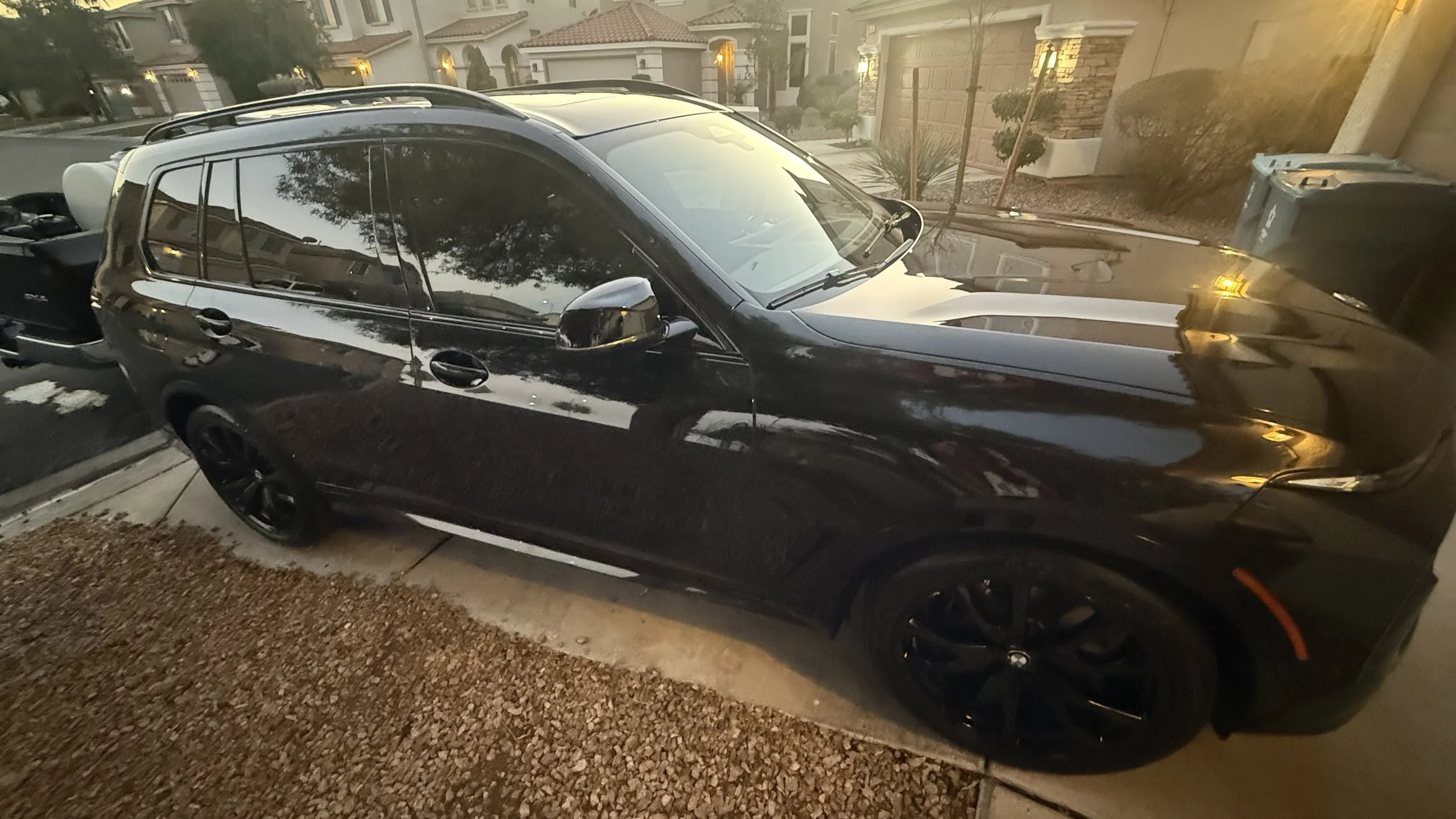 A ceramic coated black BMW SUV parked in a driveway outside a residential neighborhood during sunset. luxury mobile detail