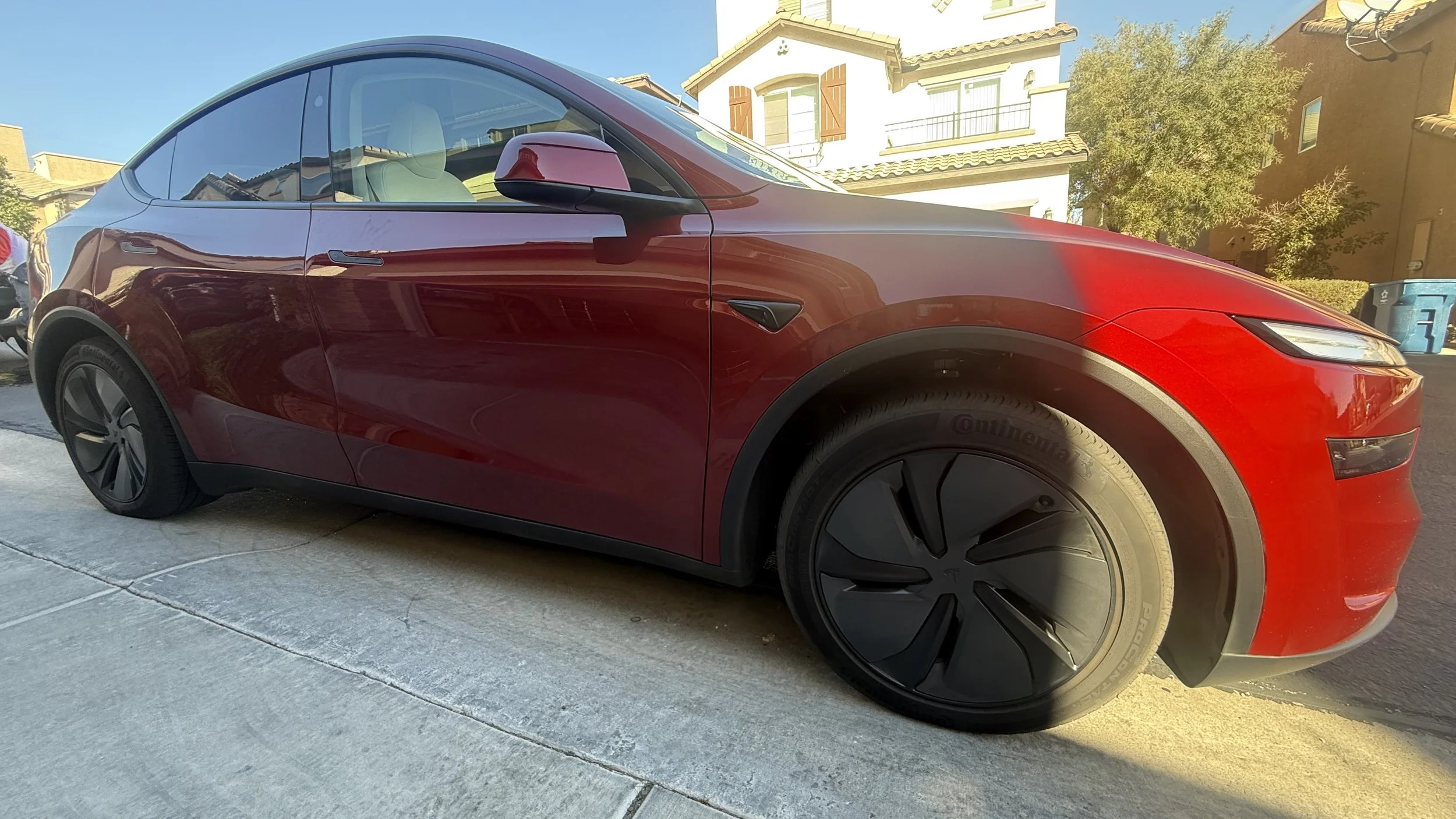 Red Tesla Model Y parked on a residential street with houses and trees in the background. Mobile car wash. Ceramic coatings.