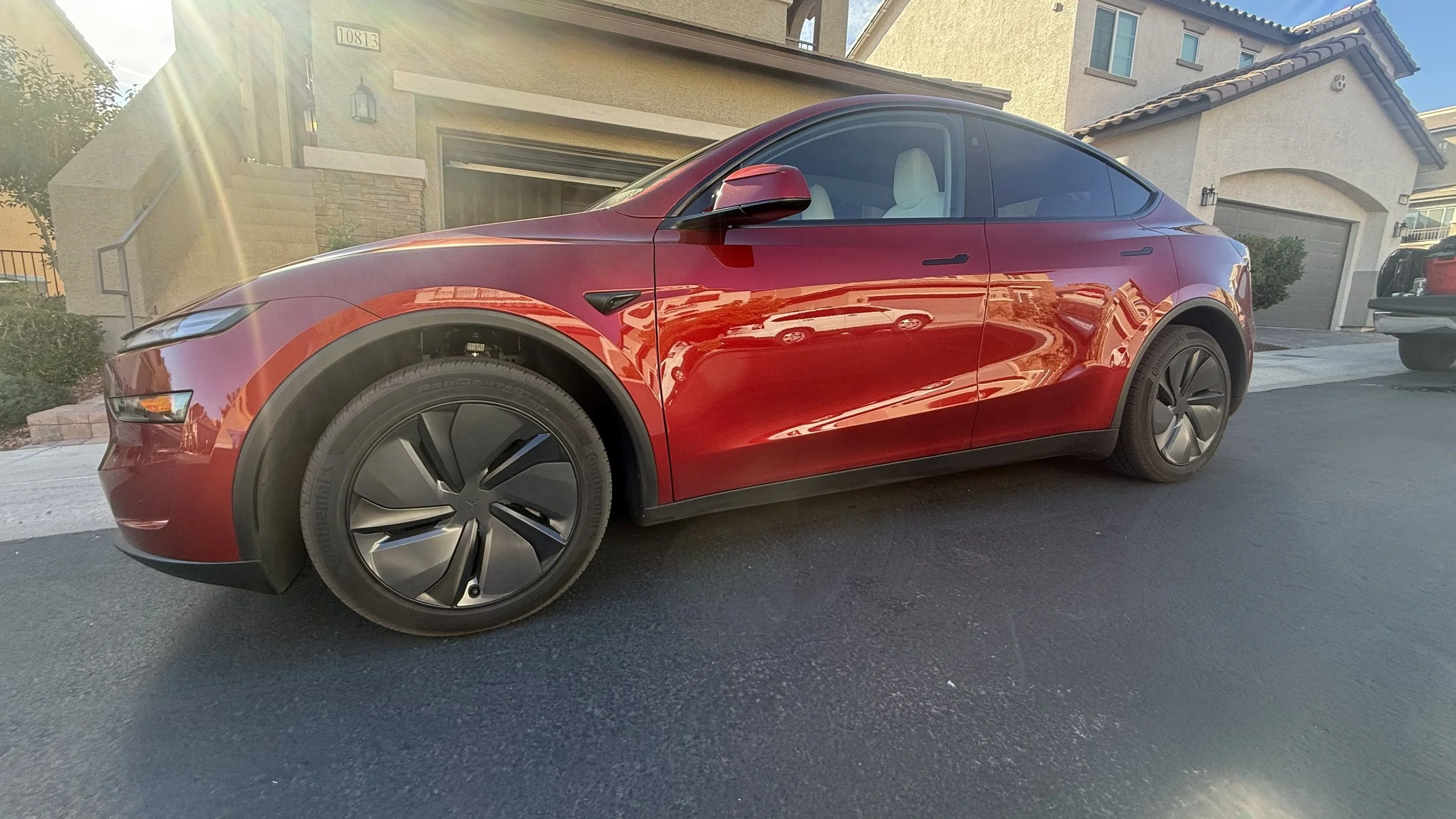 Red ceramic coated Tesla Model Y parked in front of a beige suburban house on a sunny day.