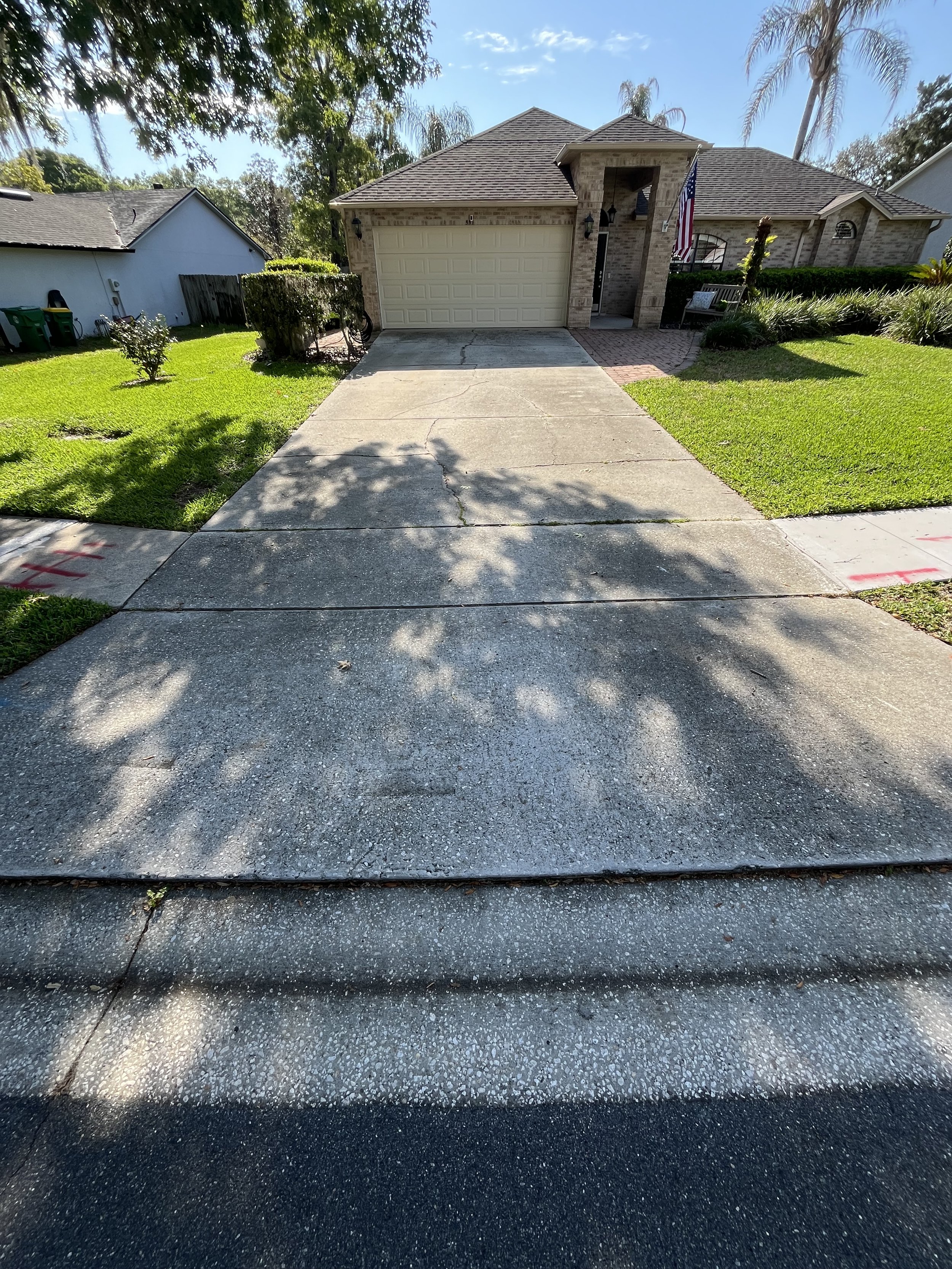 Front view of a house with a driveway, green lawn, and trees in the background on a sunny day.